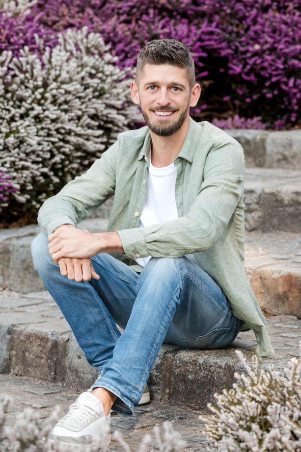 Lukas von Grünwerk sitzt auf einer Steintreppe und lächelt in die Kamera